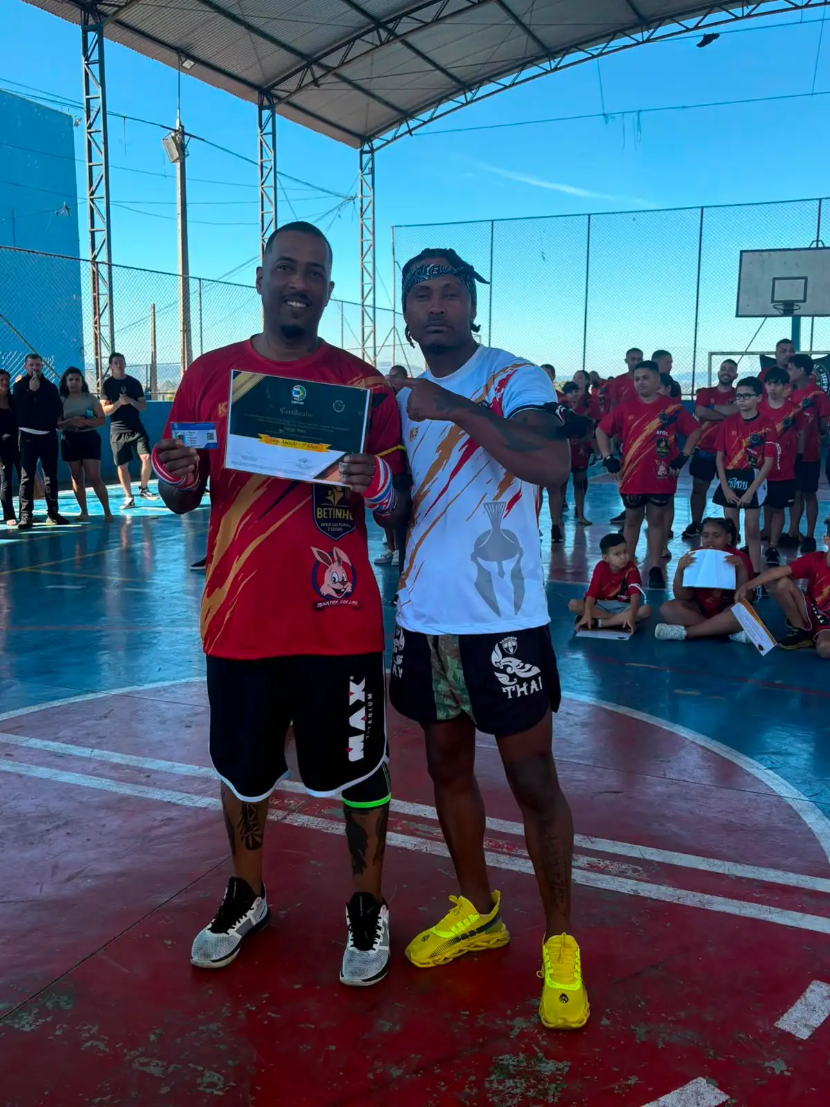 Aluno da Equipe NT Fight com o certificado de graduação ao lado do Prof. Nélsinho, na cerimônia de julho de 2026