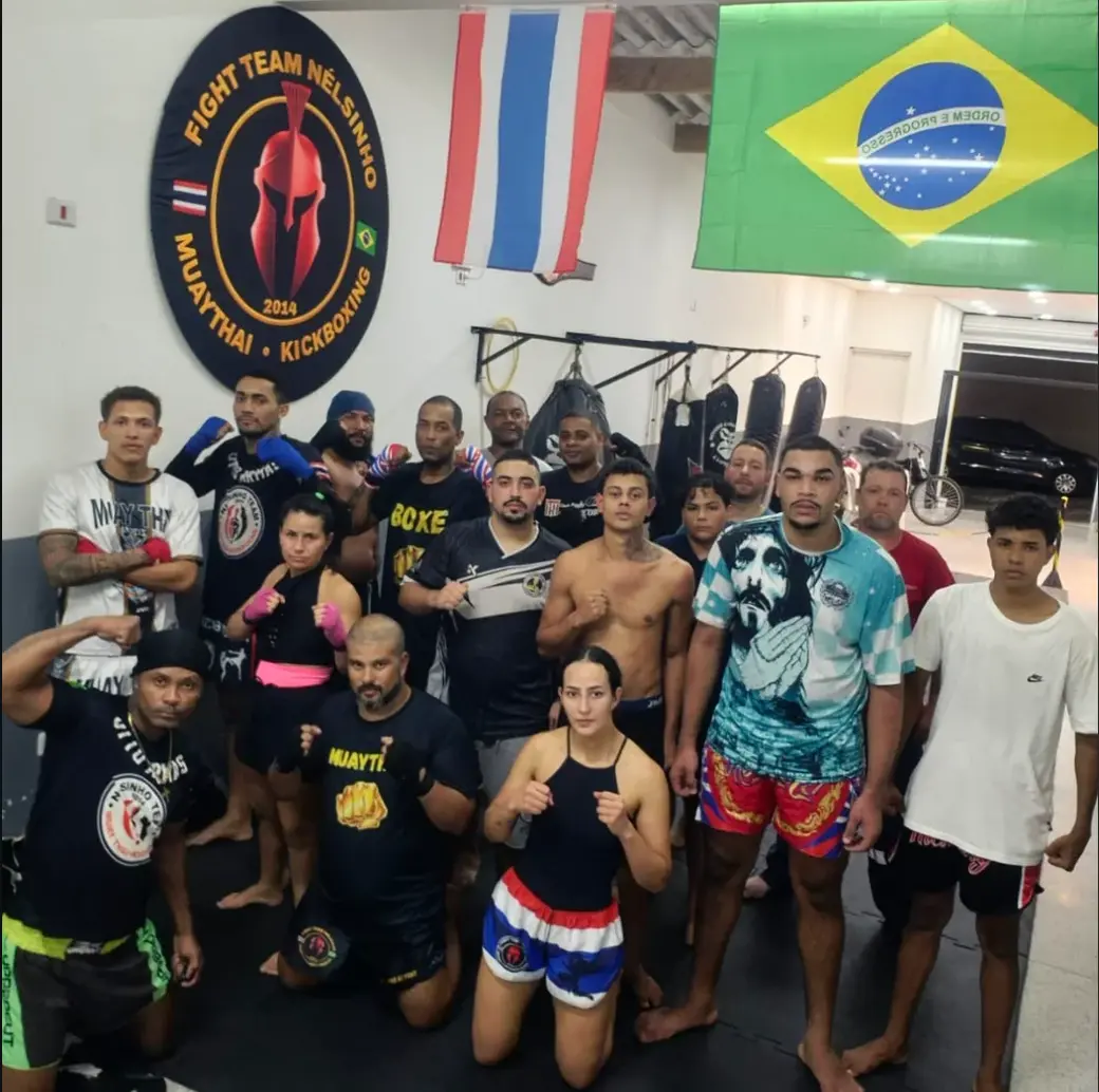 Atletas e alunos da Equipe NT Fight reunidos no CT com o brasão na parede